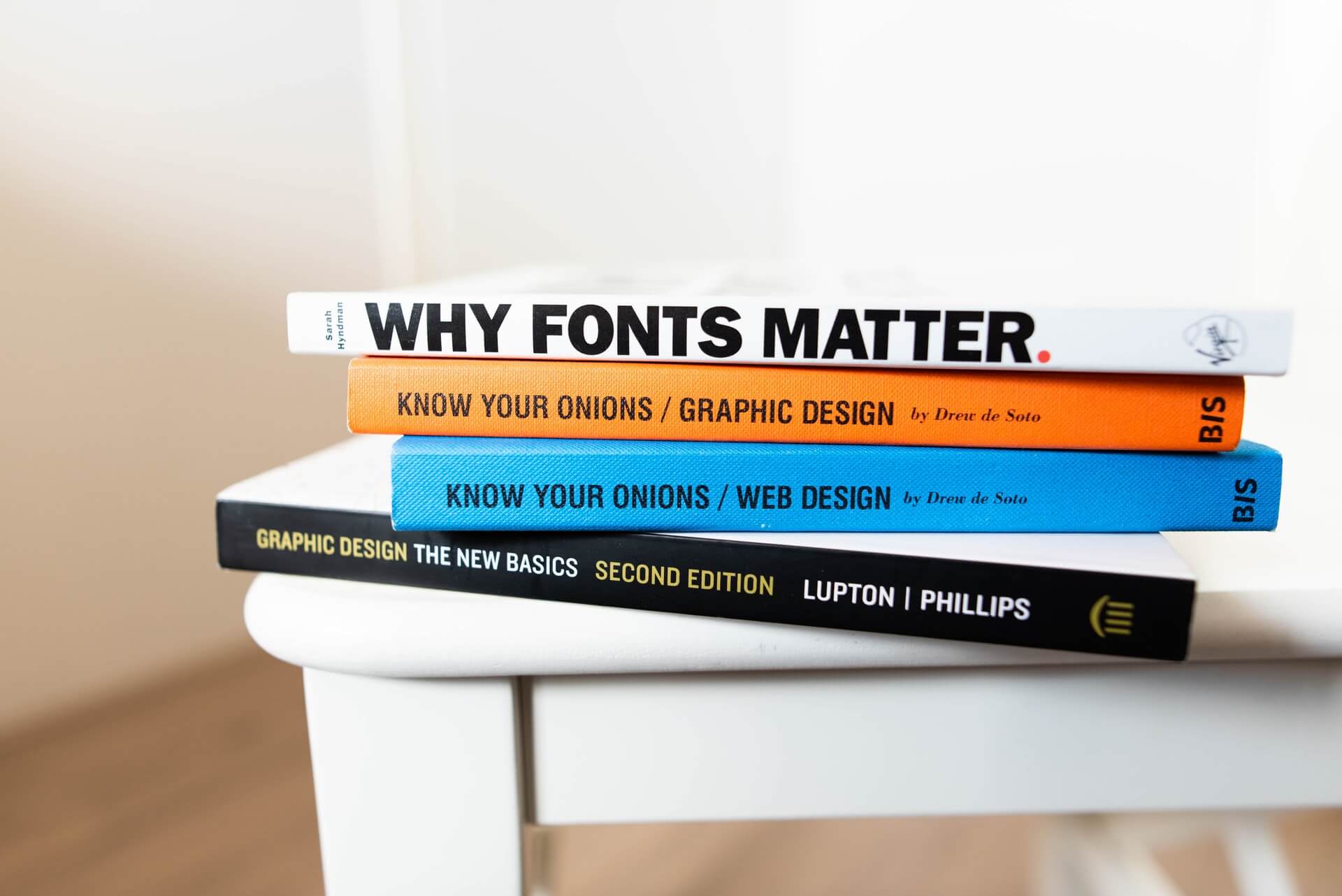 A stack of four design books titled Why Fonts Matter, Know Your Onions Graphic Design, Know Your Onions Web Design, and Graphic Design The New Basics.